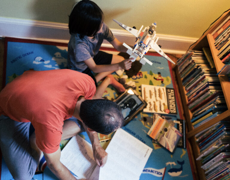 Parent and child in playroom reading and building Lego