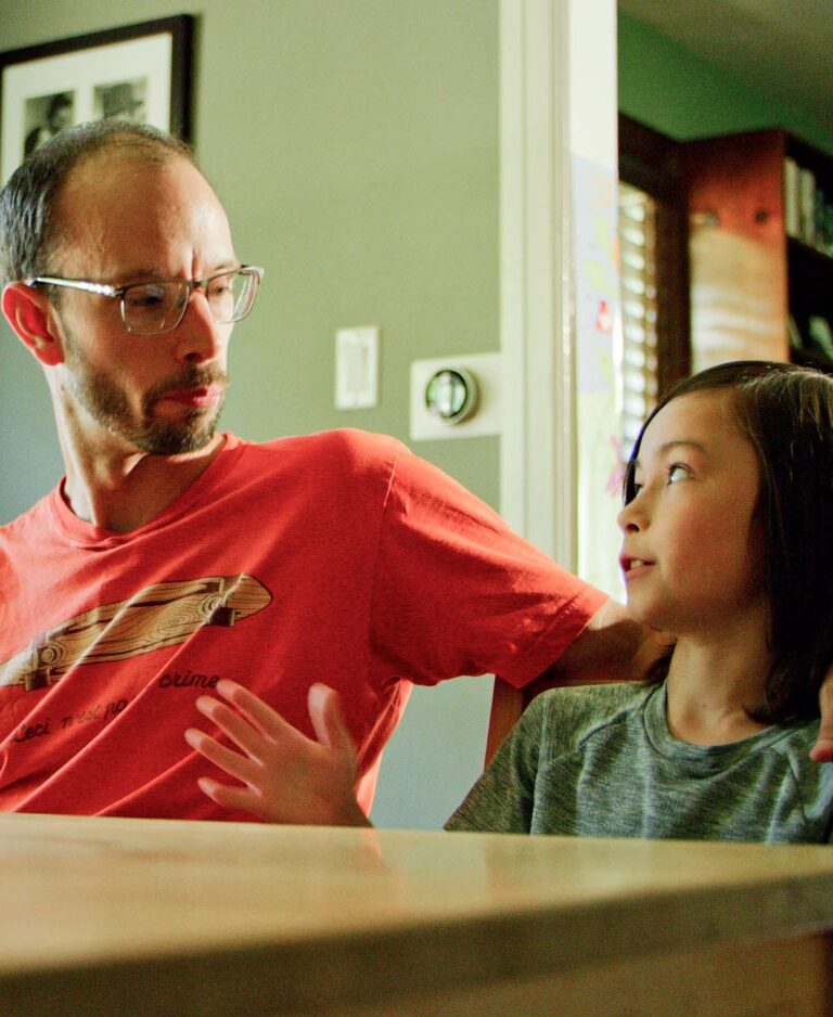 Dad and young daughter sitting at the kitchen table talking