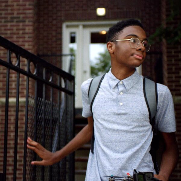 Boy coming out of his house with a backpack on.