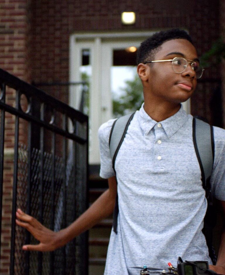 Boy coming out of his house with a backpack on.