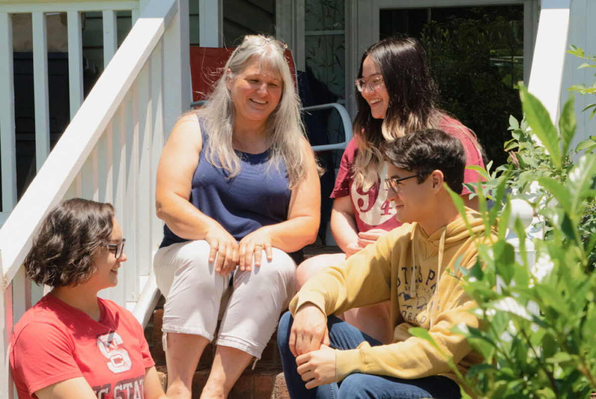 A woman sits on porch steps with her two adult daughters and adult son