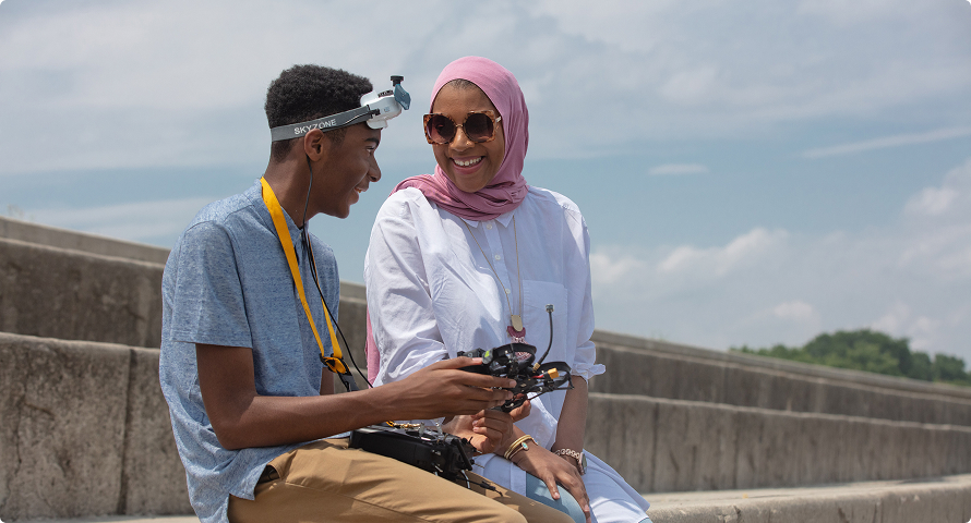 A Black woman in a hijab looks at a small drone with her teenage son