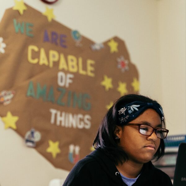 A young girl in a classroom with artwork behind her that says "We are capable of amazing things".