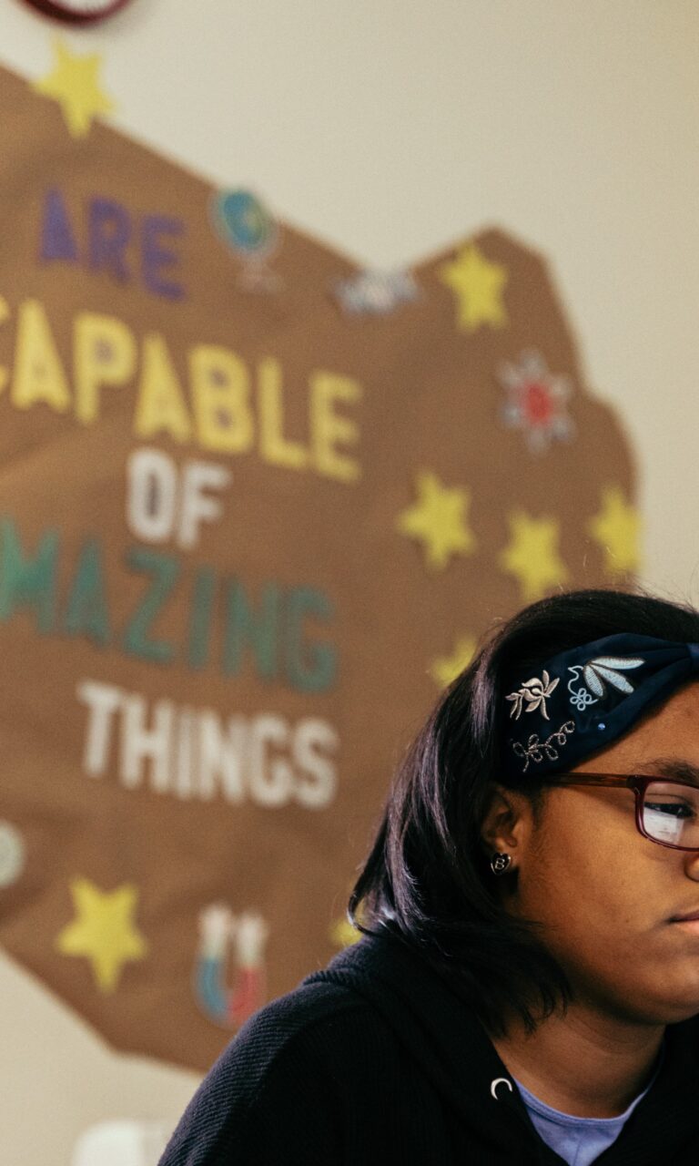 A young girl in a classroom with artwork behind her that says "We are capable of amazing things".