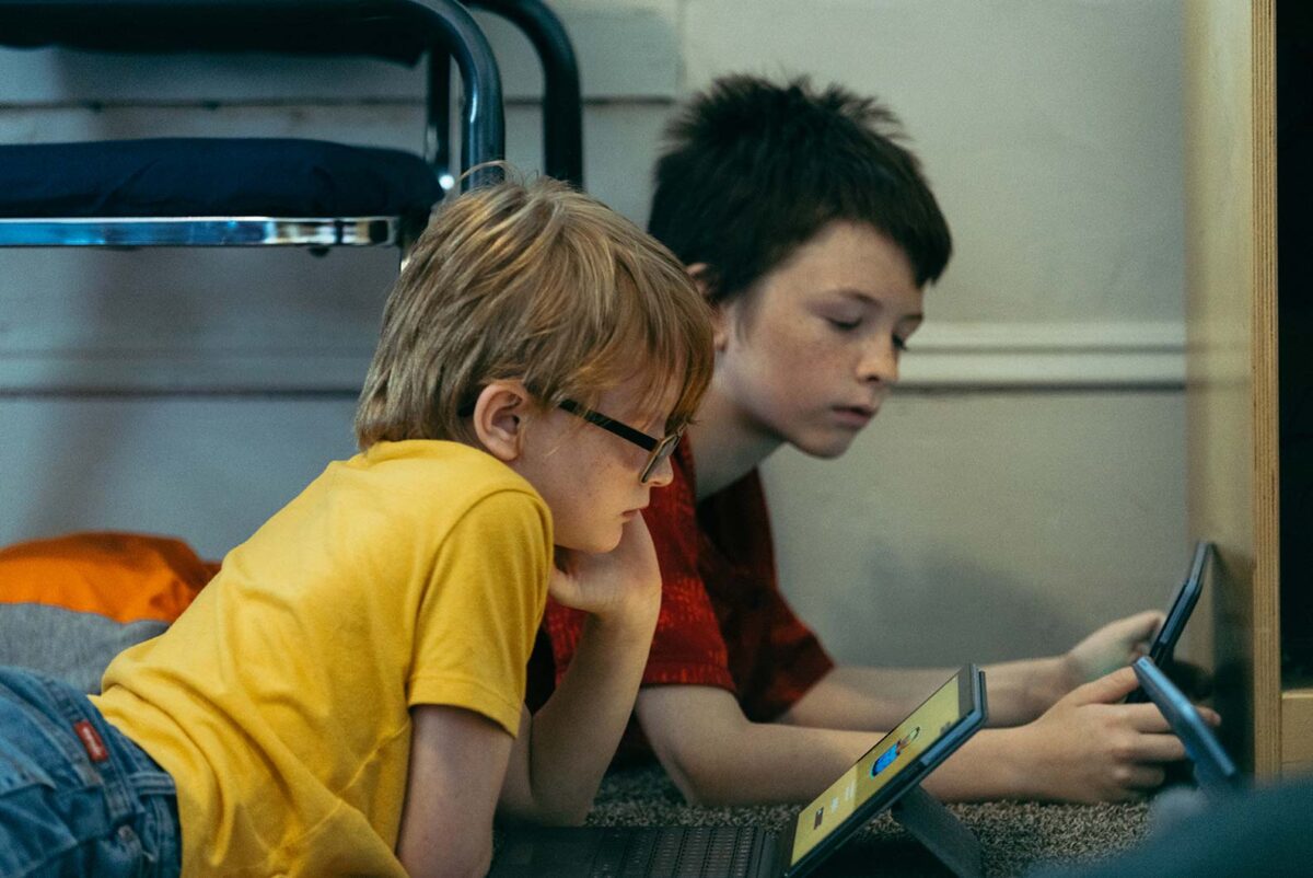 Two little boys lay on the floor and play with tablets
