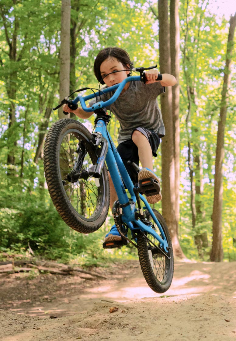 Kai on a mountain bike in a forest, popping a wheelie