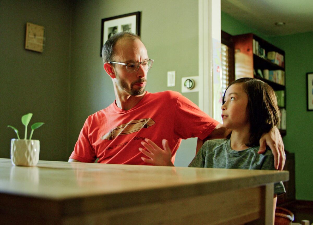 Dan with his arm around his son Kai at a kitchen table