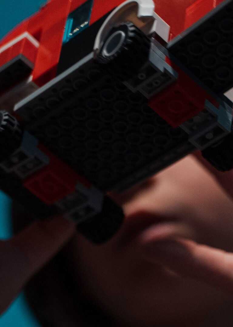 A close up of a young boy, Kai, playing with a truck made of Legos in front of his face.