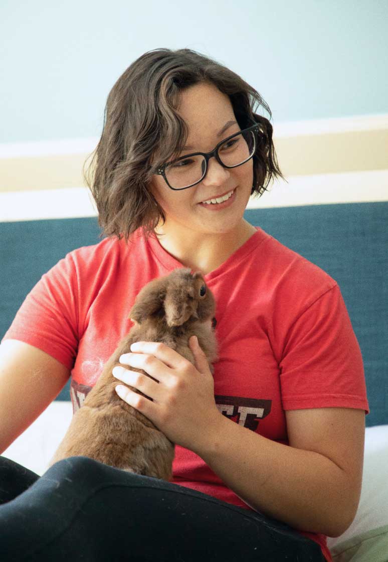 Meghan holding a rabbit in her lap and smiling at someone off-camera.