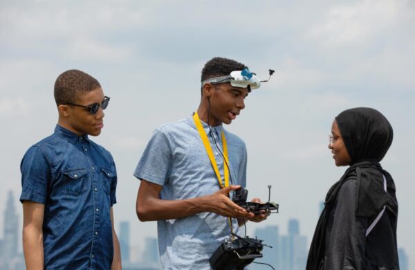 A young man holding a drone controller speaks to his brother and sister.