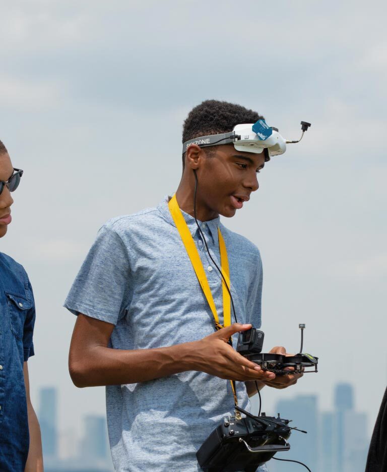 A young man holding a drone controller speaks to his brother and sister.
