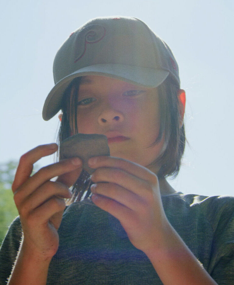 Young person outdoors examining a rock