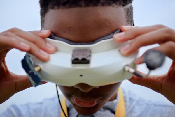A Black teenage boy looking through VR glasses with his hands on the frame.