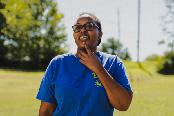 A young woman in a blue shirt in a field looking up at the sky.