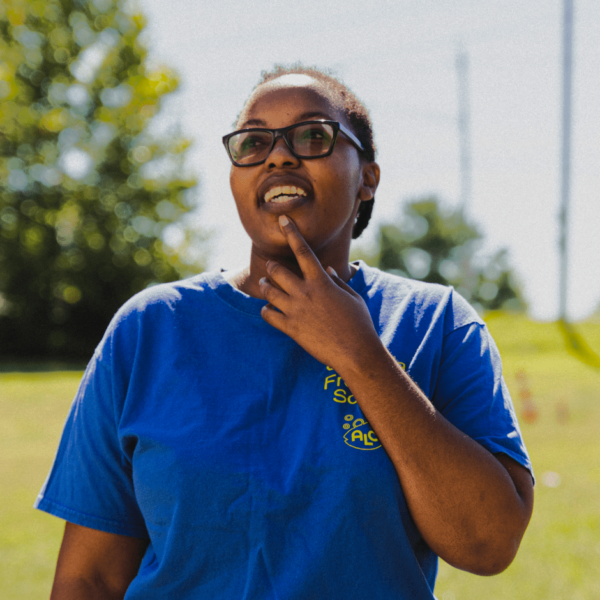 A young woman in a blue shirt in a field looking up at the sky.