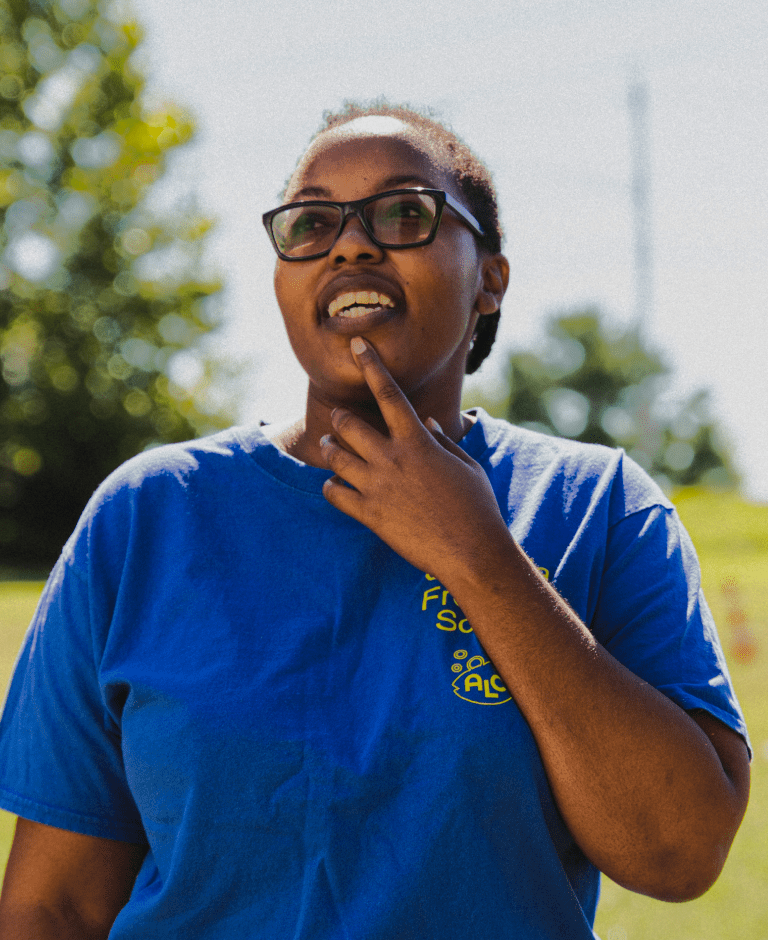 A young woman in a blue shirt in a field looking up at the sky.