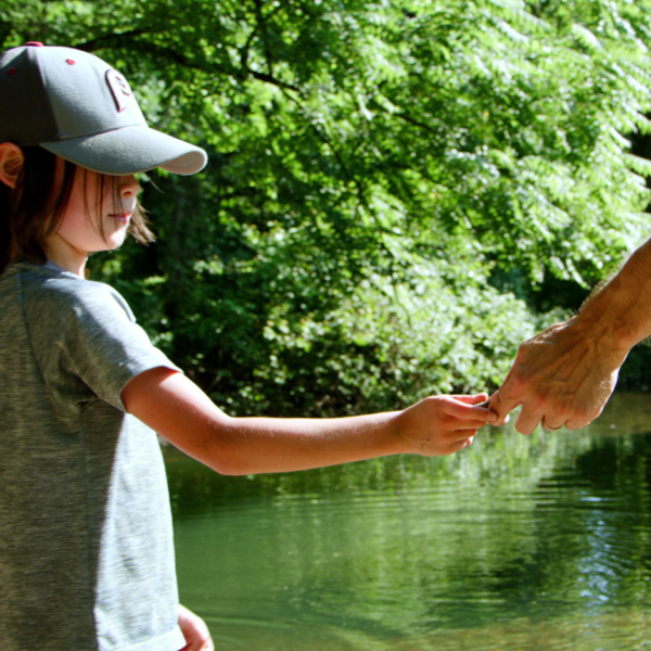 A little boy holds his father's hand by a lake