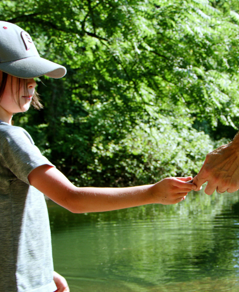 A little boy holds his father's hand by a lake