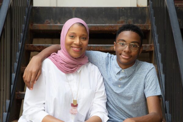 A Black mother in a hijab smiles beside her teenage son