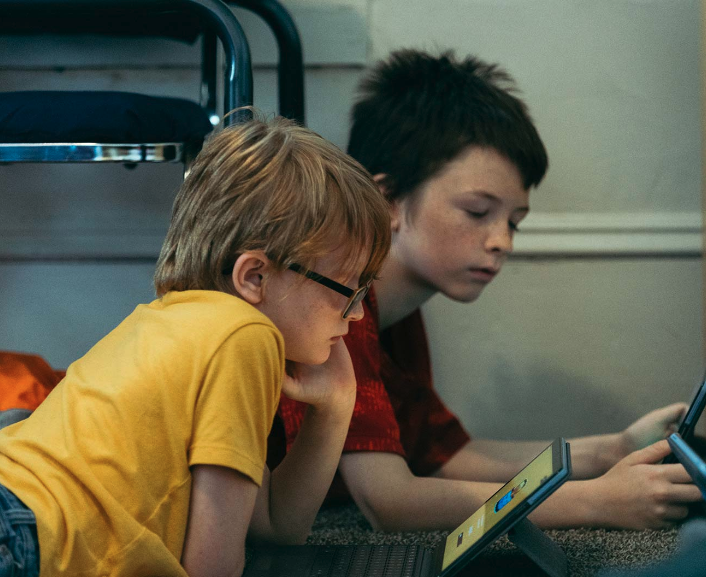 Two young boys lying in the sphinx position, watching videos on an tablet.