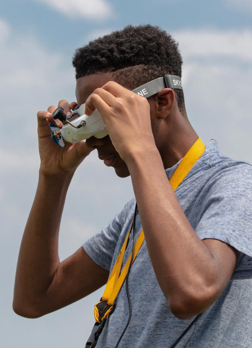 A Black teenage boy looks through drone goggles