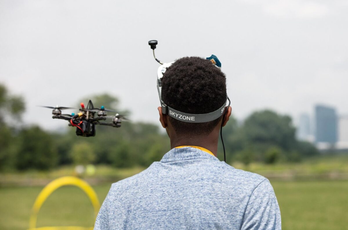 A Black teenage boy watches a drone take off over a field