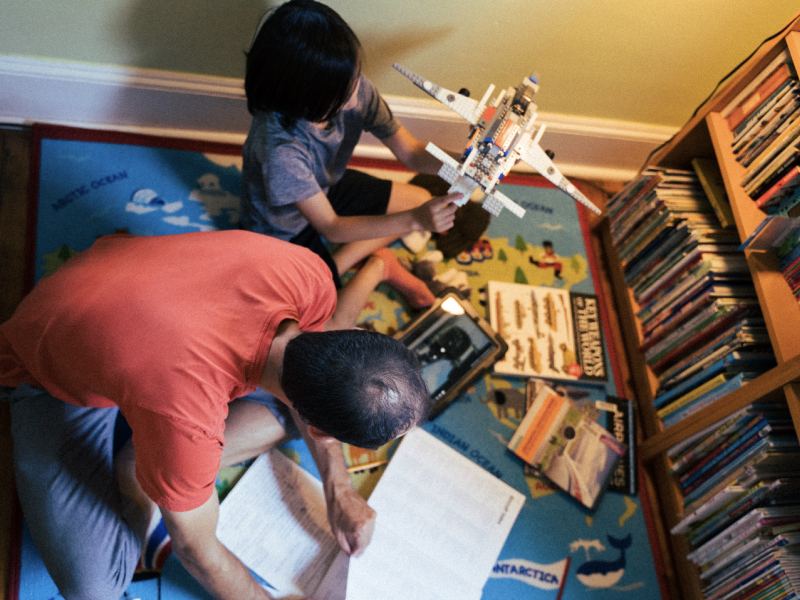 Parent and child in playroom reading and building Lego