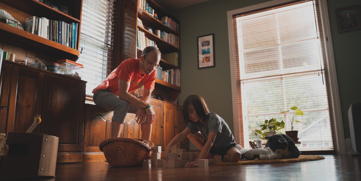 A father watches his son play with toy blocks on the floor